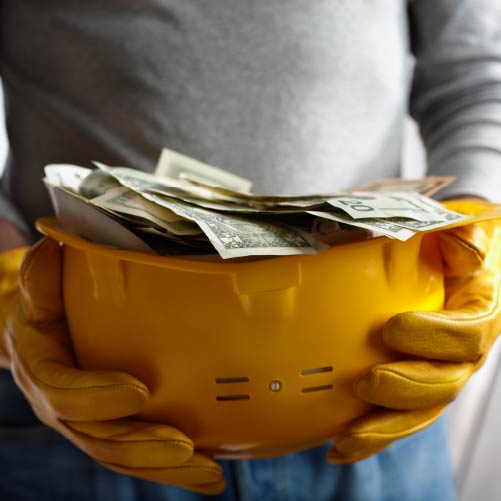 A yellow hard hat is filled with dollar bills.