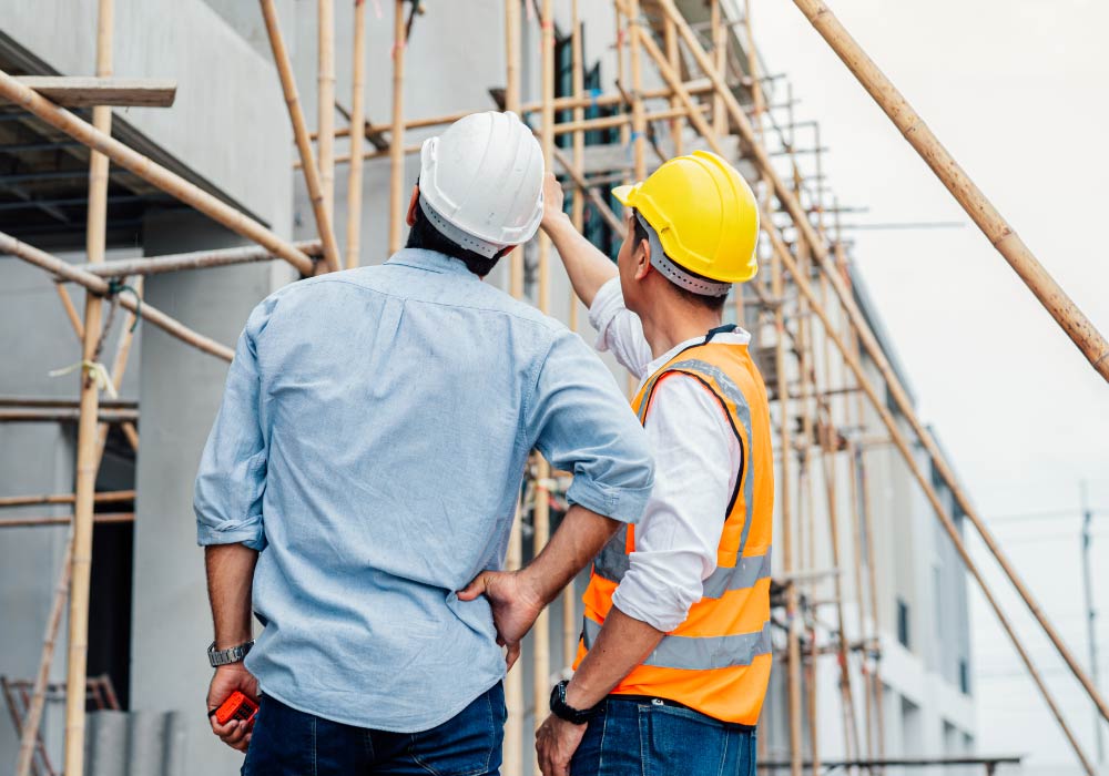 Two men wearing hard hats on a construction site and one of them is pointing to something in the distance