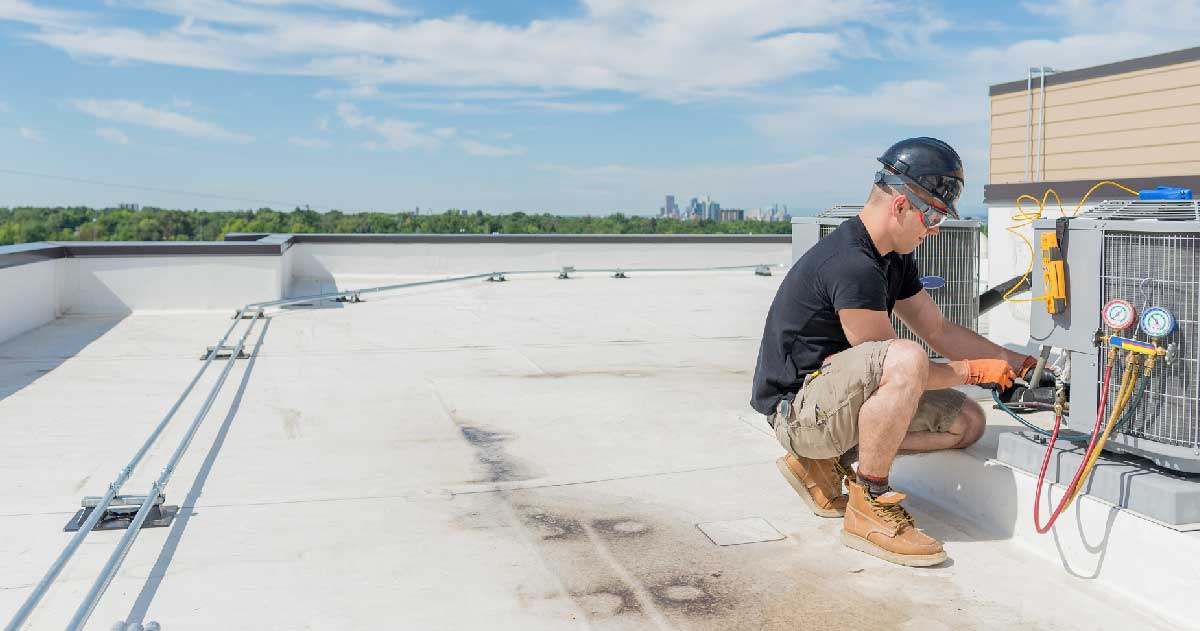 An HVAC technician is performing maintenance work on an HVAC device on a rooftop
